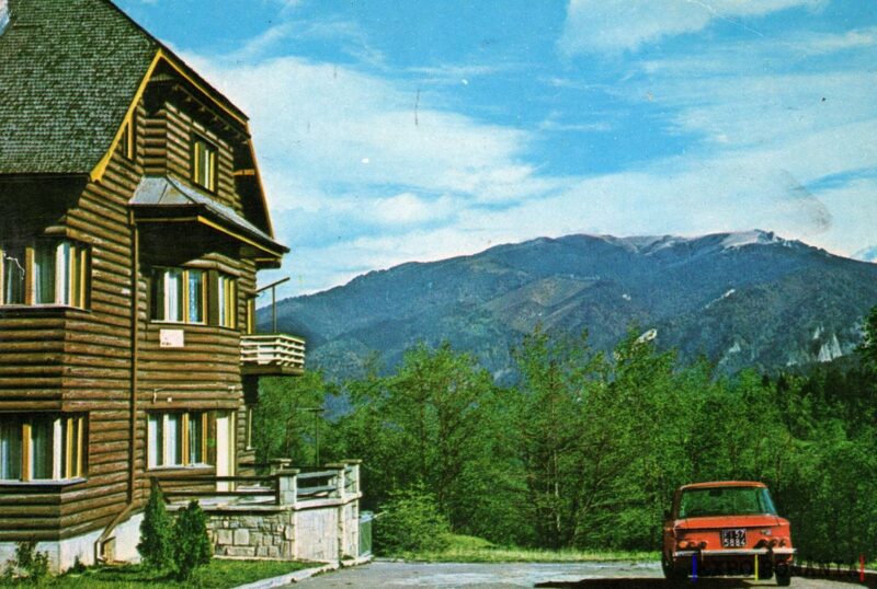 Peisaj montan cu cabană și mașină roșie